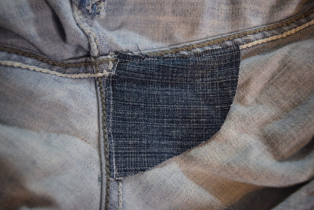 the triangular patch is sewn to one side of the back crotch within the crotch seams of the jeans