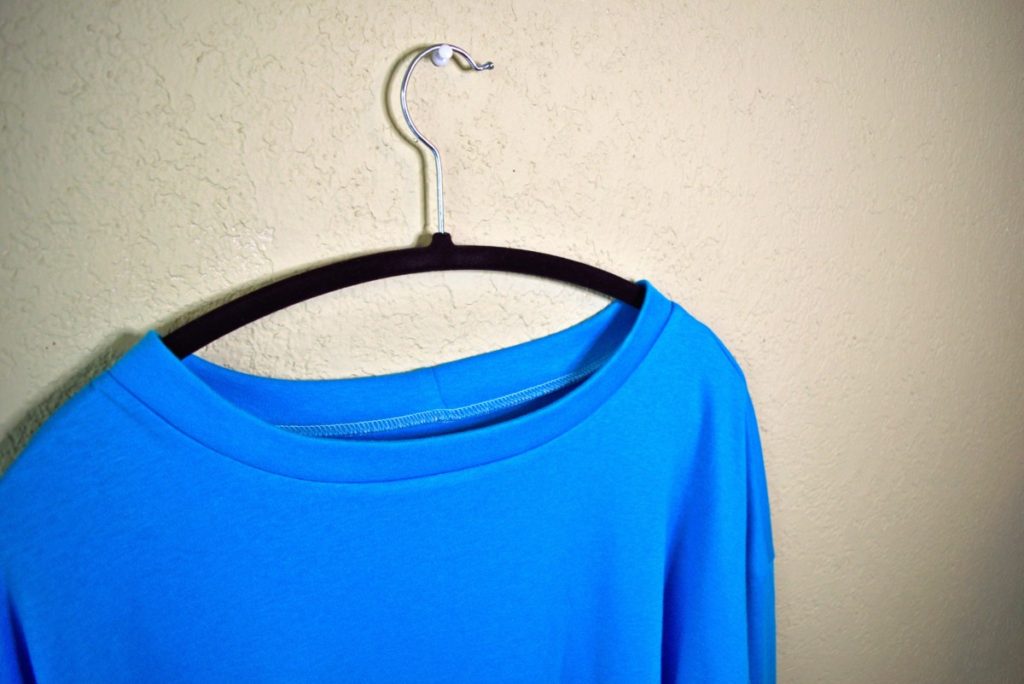 the top of a knit shirt hanging against a beige wall displaying a beautiful neckband