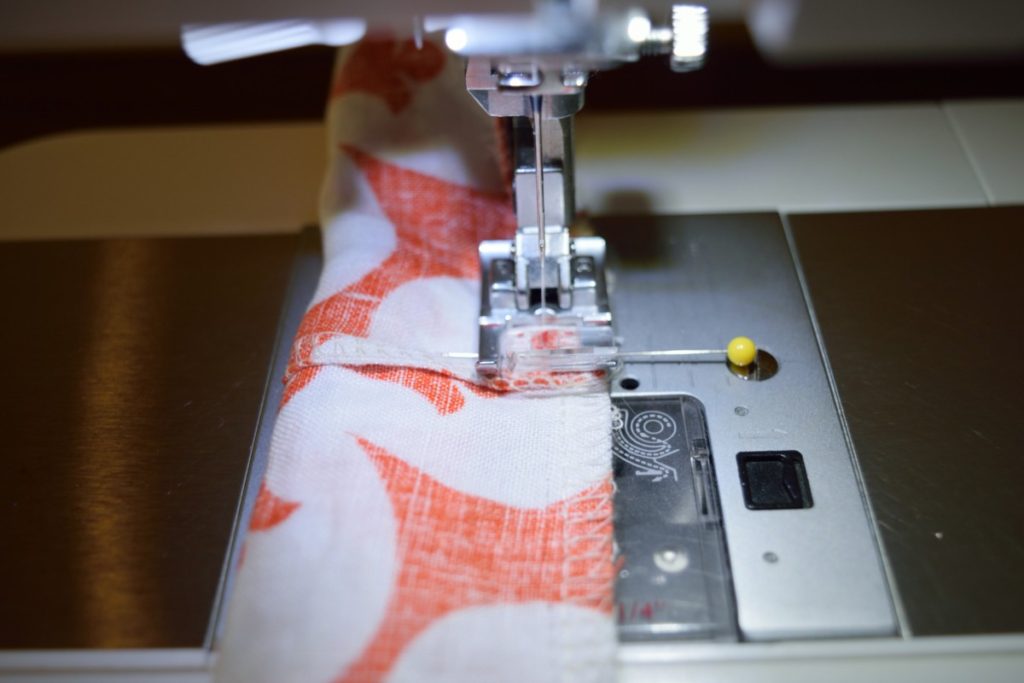 a close up of a sewing machine foot sewing an orange and white scrunchie