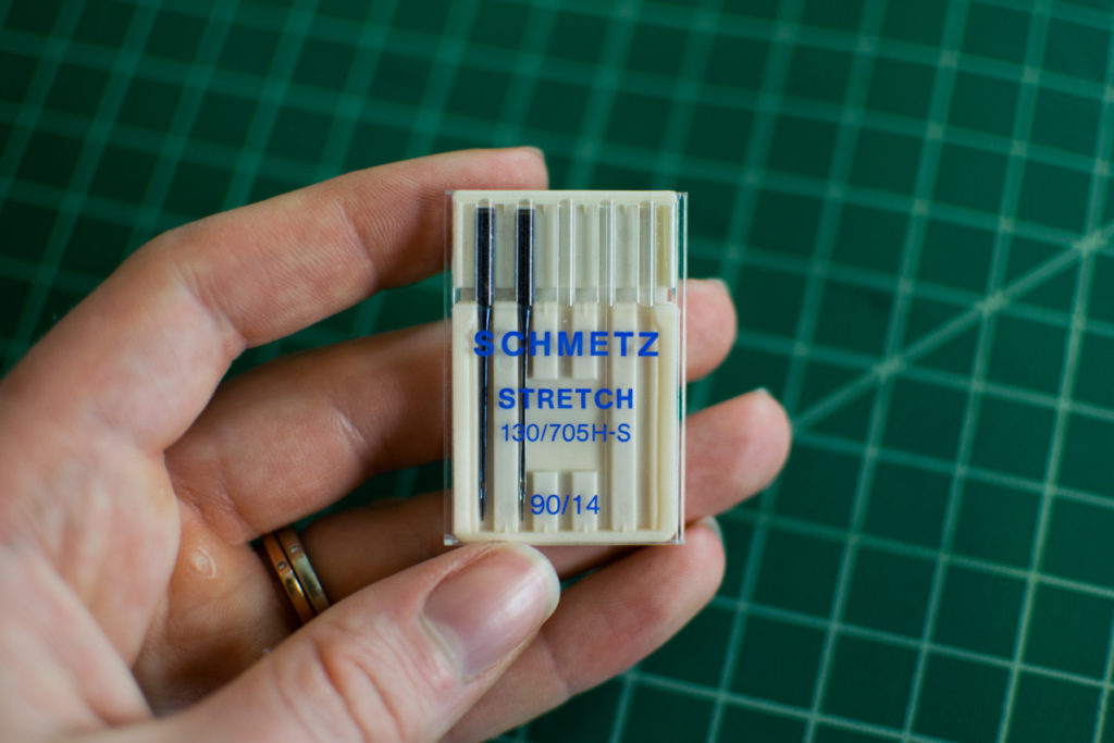 holding a pack of Schmetz stretch needles over a green cutting mat