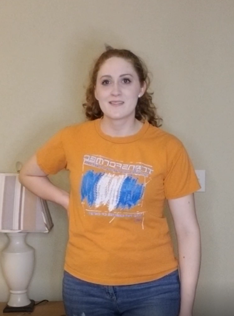 Carmen wearing an orange t shirt and jeans with hair in a ponytail
