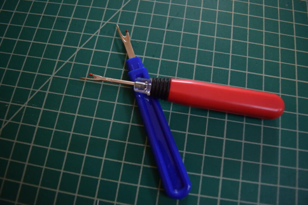 a red and a blue seam ripper laying on a green cutting mat