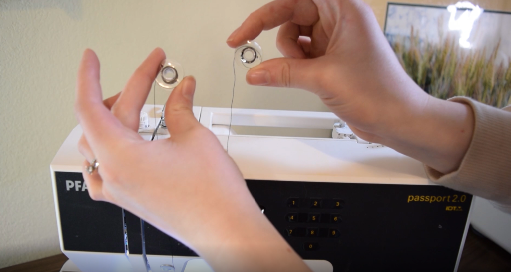 two bobbins held up in front of a sewing machine 