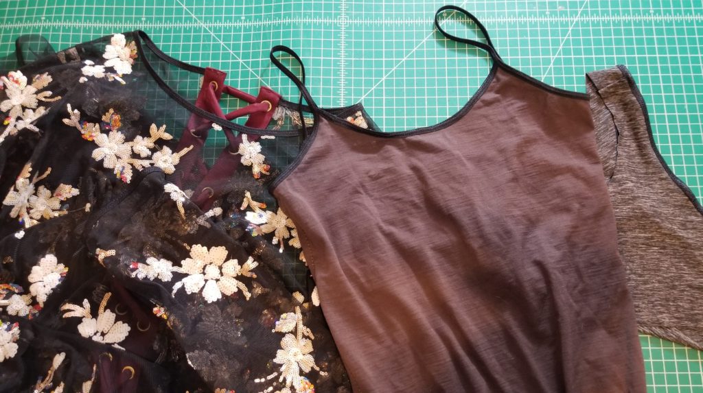 a row of three garments, on the left a sequin tulle dress, middle a brown bodysuit, right a grey sports bra, all finished with fold over elastic