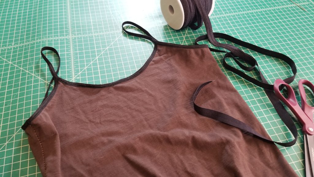 a brown body suit finished with black FOE, a roll of fold over elastic, and a pair of sewing scissors