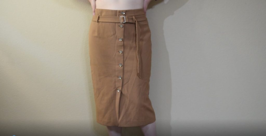 a midi length tan skirt with a row of brown buttons down the front and a belt at the waist