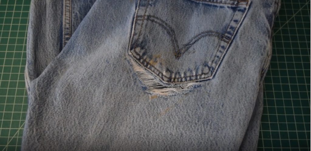 a pair of old levi's on a cutting mat with a large rip below one back pocket