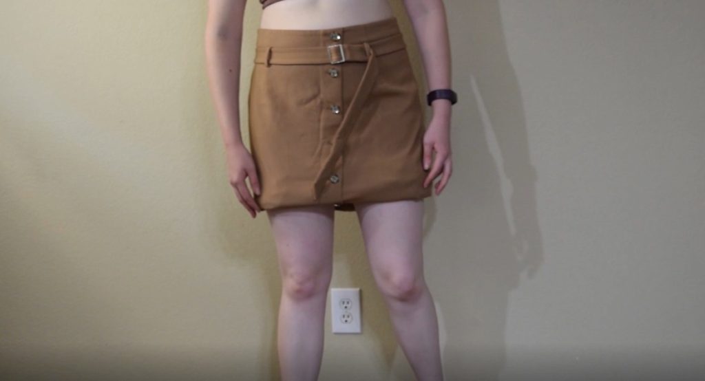 folding up a midi length tan skirt with buttons down the front to decide on the new hem